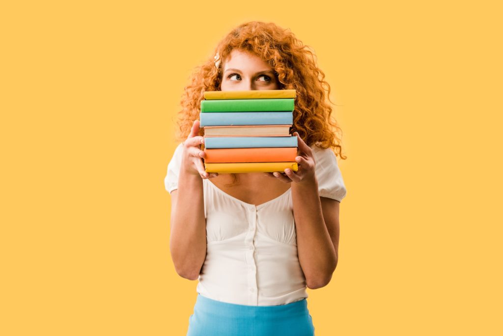 attractive female student holding books isolated on yellow
